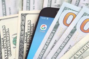 Charkov, Oekraïne - mei 2, 2021 smartphone scherm met google app en veel van honderd dollar rekeningen. bedrijf en sociaal netwerken concept foto