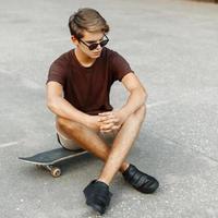 jong elegant Mens in modieus kleren rust uit Aan een skateboard. foto