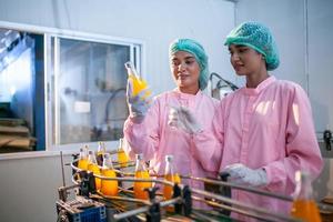 Aziatisch vrouw arbeider is controle Product flessen van fruit sap Aan de productie lijn in de drank fabriek. fabrikant cheques kwaliteit van voedsel industrie. foto