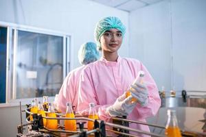 Aziatisch vrouw arbeider is controle Product flessen van fruit sap Aan de productie lijn in de drank fabriek. fabrikant cheques kwaliteit van voedsel industrie. foto