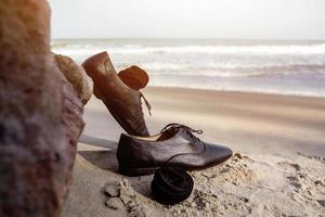 werk leven balans concept, zakenman nemen uit zijn werken Oxford schoenen en vertrekken het Aan de zand strand in de buurt de rots voor wandelen in de zee. lucht en Golf net zo achtergrond foto