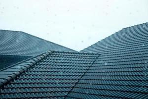 regen is vallend in blauw tegels dak. schot Aan regenachtig dag. behuizing en architectuur. weer en seizoen verandering foto