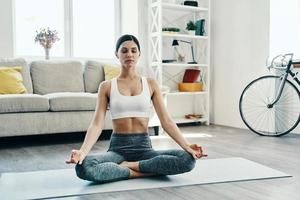 ontspannende oefening. mooi jong vrouw in sport- kleding beoefenen yoga terwijl uitgeven tijd Bij huis foto