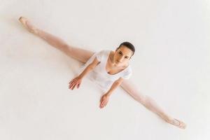 het duurt discipline naar worden de het beste. top visie van jong ballerina in wit tutu aan het doen splitst foto