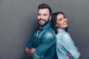 gelukkig liefhebbend paar. studio schot van mooi jong paar in jeans slijtage staand terug naar terug en glimlachen foto