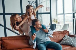 vrolijk jong familie glimlachen en omarmen terwijl bonding samen Bij huis foto