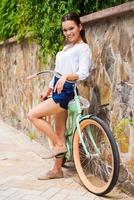 jong en zorgeloos. vol lengte van mooi jong vrouw leunend Bij haar wijnoogst fiets en glimlachen foto