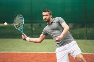 zelfverzekerd tennis speler. zelfverzekerd jong Mens in sport- kleren spelen tennis Aan tennis rechtbank foto