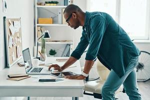 bedrijf deskundige. knap jong Afrikaanse Mens in overhemd gebruik makend van laptop terwijl staand in de kantoor foto