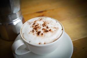 heet cappuccino in wit kop met houten achtergrond, koffie is een populair drinken allemaal over- de wereld. foto