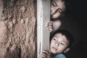 detailopname arm jongen gluren uit van een vervallen huis, concept van bijstand naar de arm, menselijk rechten. foto