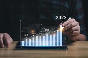 bedrijf groei en vooruitgang concept. zakenman is tonen virtueel hologram tabel van tablet. plannen naar toenemen bedrijf groei en een toenemen in de indicatoren van positief groei in 2022 foto