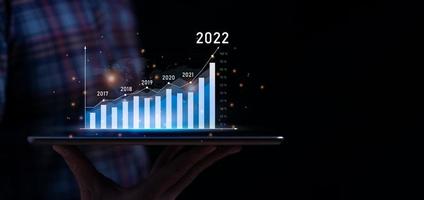 bedrijf groei en vooruitgang concept. zakenman is tonen virtueel hologram tabel van tablet. plannen naar toenemen bedrijf groei en een toenemen in de indicatoren van positief groei in 2022 foto