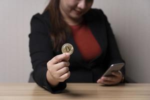 bedrijf vrouw Holding bitcoins en transacties cryptogeld Aan haar smartphone. concept cryptogeld aandelenbeurs. technologie en investering digitaal. financiën, investeerder, verzamelen geld, hoog investering risico foto