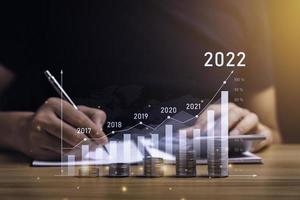 zakenman planning 2022 bedrijf groei Aan bureau met virtueel hologram tabel grafiek. berekenen inkomen en winst Aan investeringen en een toenemen in de indicatoren van positief groei foto