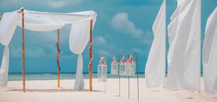 droom romantisch strand bruiloft decoratie, wit zand en blauw bewolkt lucht. paar liefde huwelijksreis en verjaardag viering, zonnig zacht pastel gekleurde instelling, bloemen en kaarsen onder wit gordijnen foto