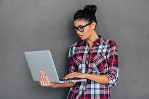 vrouw met laptop. mooi jong vrouw werken Aan laptop terwijl staand tegen grijs achtergrond foto