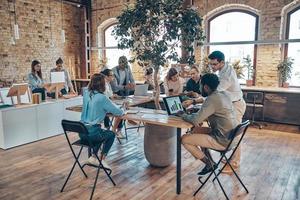 groep van jong modern mensen in slim gewoontjes slijtage communiceren en gebruik makend van modern technologieën terwijl werken in de kantoor foto