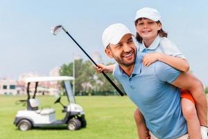 dat was een mooi zo spel. vrolijk jong Mens meeliften zijn zoon terwijl staand Aan golf Cursus foto