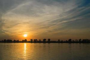 helder oranje zonsondergang Bij rivier- foto