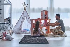 gebruik makend van verbeelding. vader en dochter spelen met een poppenhuis samen terwijl zittend Aan de verdieping in slaapkamer foto