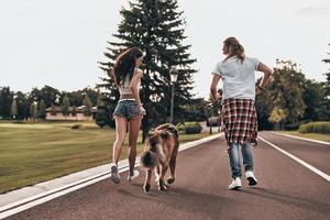 speels en gevulde met liefde. vol lengte achterzijde visie van mooi jong paar rennen met hun hond terwijl uitgeven tijd buitenshuis foto