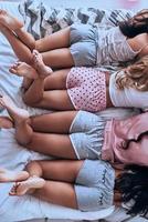 schoonheden. dichtbij omhoog top visie van vier jong Dames in pyjama houden voet verheven terwijl aan het liegen Aan de bed foto
