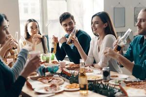 ontspannende avond. groep van jong mensen in gewoontjes slijtage aan het eten pizza en glimlachen terwijl hebben een avondeten partij binnenshuis foto