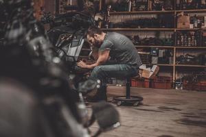 uitgeven tijd met Fietsen. zelfverzekerd jong Mens repareren motorfiets in reparatie winkel foto