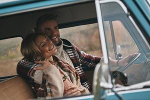 gemakkelijk vreugde van liefdevol. mooi jong paar omarmen en glimlachen terwijl zittend in retro stijl mini busje foto