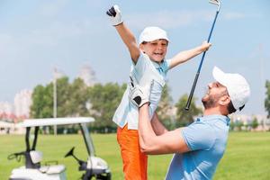 vreugde van Super goed spel. opgewonden jong Mens plukken omhoog zijn zoon terwijl staand Aan de golf Cursus foto