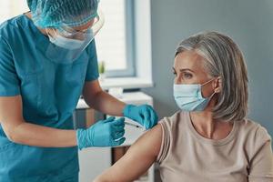 vrouw verpleegster in beschermend werkkleding maken coronavirus vaccinatie naar volwassen vrouw terwijl werken in de ziekenhuis foto