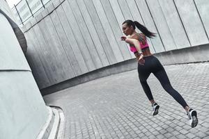 vastbesloten naar winnen. vol lengte van jong vrouw in sport- kleding jogging terwijl oefenen buitenshuis foto