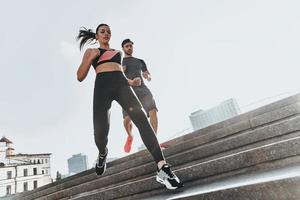 werken uit Aan de trap. laag hoek visie van jong paar in sport kleding rennen naar beneden de trap samen foto