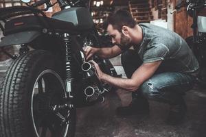 Mens vaststelling fiets. zelfverzekerd jong Mens repareren motorfiets in de buurt zijn garage foto