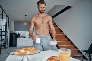 mooi zo op zoek jong zonder shirt Mens hebben ontbijt terwijl uitgeven tijd Bij huis keuken foto