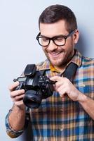 instelling de camera. portret van zelfverzekerd jong Mens in overhemd Holding camera terwijl staand tegen grijs achtergrond foto