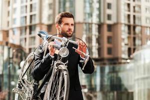 Aan de manier naar zijn werk.vertrouwen jong zakenman draag- zijn fiets Aan schouder terwijl kruispunt de weg foto