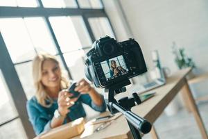 mooi jong vrouw in gewoontjes kleding glimlachen terwijl werken in voorkant van digitaal camera foto