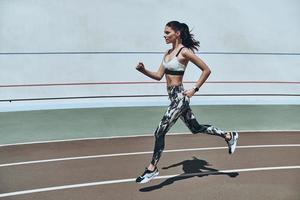 sport is de manier van leven. vol lengte van jong vrouw in sport- kleding jogging terwijl oefenen buitenshuis foto