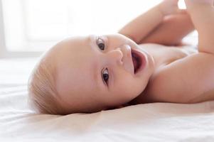 gelukkig baby. gelukkig weinig baby glimlachen Bij camera terwijl aan het liegen in bed foto