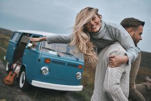 gevoel vrij naar Doen iets. knap jong Mens draag- zijn aantrekkelijk vriendin Aan schouders en glimlachen terwijl staand in de buurt de blauw retro stijl mini busje foto