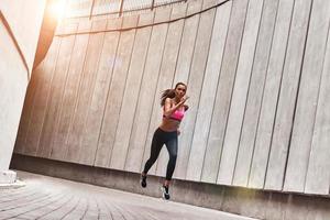 vol van energie. vol lengte van jong vrouw in sport- kleding jogging terwijl oefenen buitenshuis foto
