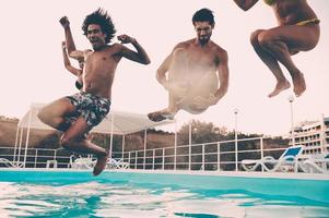 zwembad tijd. groep van mooi jong mensen op zoek gelukkig terwijl jumping in de zwemmen zwembad samen foto