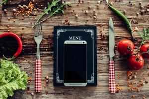telefoontje voor voedsel. top visie van schoolbord menu met slim telefoon houdende Aan de rustiek houten bureau met groenten in de omgeving van foto