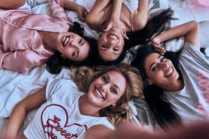 waar vrouwelijk schoonheid. top visie zelf portret van vier aantrekkelijk jong Dames in pyjama glimlachen en op zoek Bij camera terwijl aan het liegen Aan de bed Bij huis foto