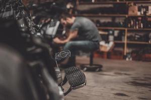 repareren fiets. zelfverzekerd jong Mens repareren motorfiets in reparatie winkel foto