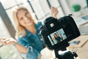 mooi jong vrouw glimlachen en gebaren terwijl zittend in voorkant van digitaal camera foto