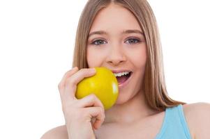 aan het eten een vers appel. vrolijk tiener- meisje aan het eten groen appel en glimlachen terwijl staand geïsoleerd Aan wit foto
