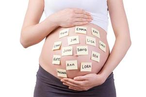 baby namen Aan haar buik. bijgesneden beeld van zwanger vrouw met baby namen Aan haar buik staand geïsoleerd Aan wit foto